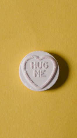 Vertical-Video-Close-Up-Of-Vertical-Video-Of-Hand-Holding-Heart-Candy-With-True-Love-Message-On-Yellow-Background